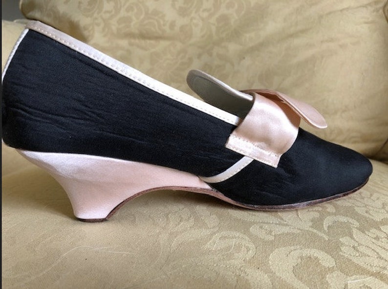 May include: Black satin heeled shoe with a pink satin bow and trim. The heel is a pink wedge.