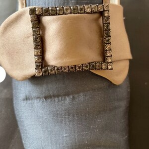 May include: A close-up of a beige satin shoe with a large, rectangular buckle adorned with clear rhinestones.