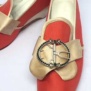 May include: A pair of red satin shoes with gold bows and jeweled buckles. The shoes have pointed toes and a low heel.