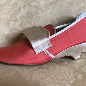 May include: A pair of coral pink satin heeled shoes with a beige satin strap across the top.