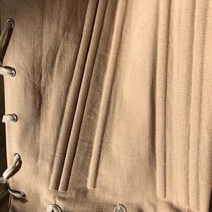 Puede incluir: Primer plano de un cors&eacute; beige con ballenas verticales y ojales para atar. La tela tiene un aspecto texturizado, y el cors&eacute; est&aacute; dise&ntilde;ado con una silueta estructurada. Los ojales est&aacute;n reforzados con anillos met&aacute;licos.