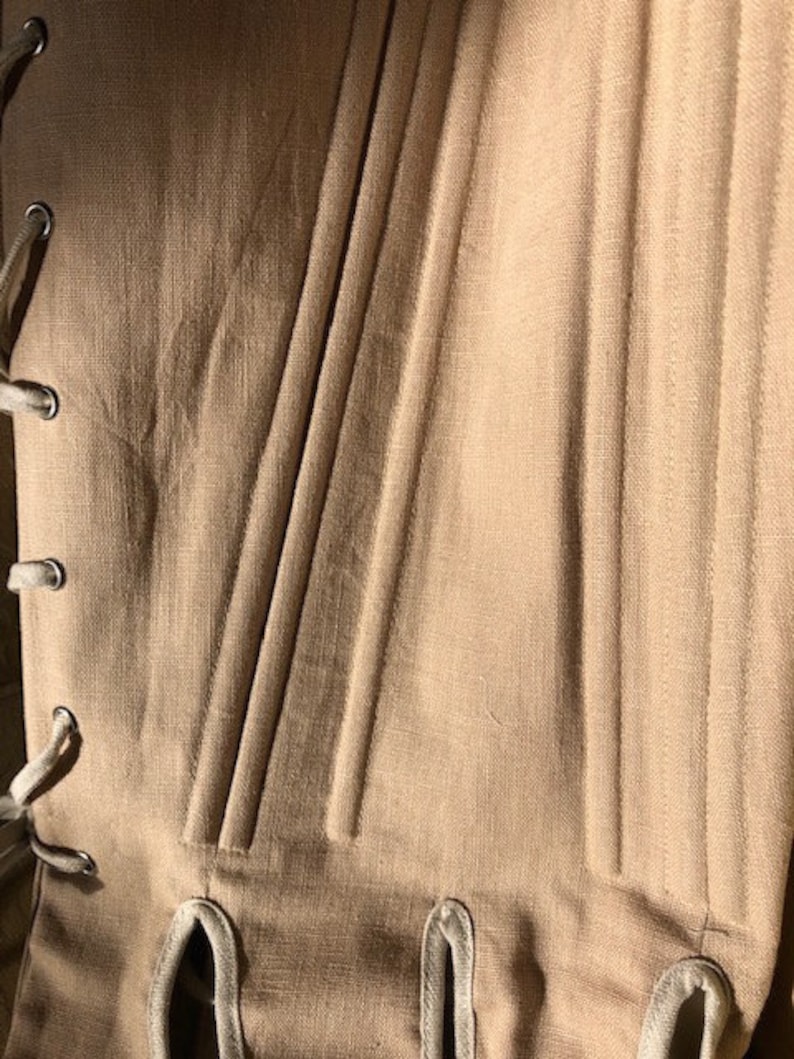 Puede incluir: Primer plano de un cors&eacute; beige con ballenas verticales y ojales para atar. La tela tiene un aspecto texturizado, y el cors&eacute; est&aacute; dise&ntilde;ado con una silueta estructurada. Los ojales est&aacute;n reforzados con anillos met&aacute;licos.