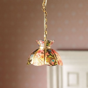 Può includere: Una catena dorata pende dal soffitto, sostenendo un paralume con motivo floreale. Il paralume è realizzato in carta e ha un bordo dorato.