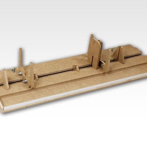 Puede incluir: Un jig de madera para construir maquetas de aviones. El jig tiene una serie de ranuras y soportes para sujetar la maqueta mientras se pega.