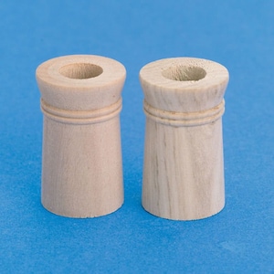 Puede incluir: Dos portavelas de madera sin terminar con una ranura decorativa alrededor de la parte superior. Los portavelas son de color marrón claro y tienen un acabado liso y pulido.