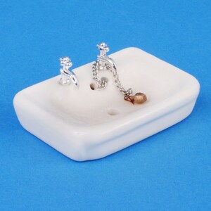 May include: A white porcelain dollhouse sink with two silver taps and a silver chain with a brown stopper.