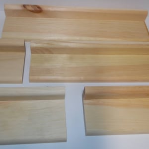 May include: Four pieces of unfinished wood trim, each with a different shape and size. The trim is made of light-colored wood and has a smooth surface.