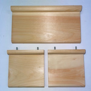 May include: Three wooden shelves with rounded edges. The top shelf is larger than the two bottom shelves, which are the same size. The shelves are made of light wood and have a natural finish.