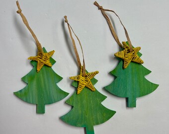 Könnte beinhalten: Drei Weihnachtsbaumschmuck aus Holz mit grün-gelber Lackierung. Jeder Baum hat einen geflochtenen gelben Stern und eine braune Papierschnur zum Aufhängen. Festlicher Weihnachtsschmuck.