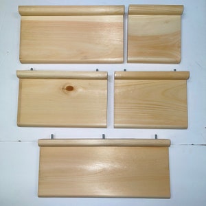 May include: Five unfinished wooden shelves with a natural wood grain. Each shelf has a rounded edge at the top and is rectangular. The shelves are of varying sizes and are ready for staining or painting.