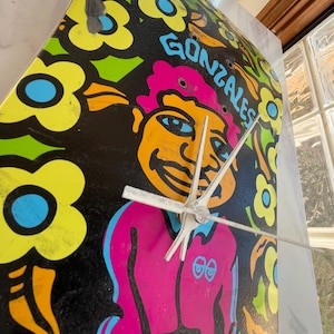 May include: A black and yellow skateboard clock featuring a cartoon face and the word "GONZALES" printed on it. The clock has silver hands and a black background with colourful flowers.