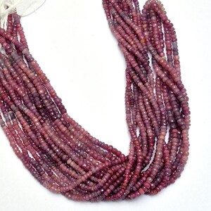 May include: A strand of pink ruby beads, faceted and round, strung on a white thread. The beads are approximately 3mm in diameter and are arranged in a loose, flowing pattern.