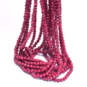 Può includere: Una collana di perline di pietra preziosa sfaccettata rosso scuro. Le perline sono rotonde e hanno una superficie testurizzata.