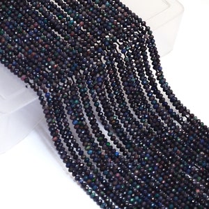 May include: Strands of black faceted beads with iridescent flashes of color. The beads are small and strung together, creating a flowing, textured appearance. The beads are likely used for jewelry making.