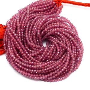 May include: A strand of pink gemstone beads, faceted and round, strung on a red thread. The beads are approximately 4mm in diameter and are arranged in a circular pattern.