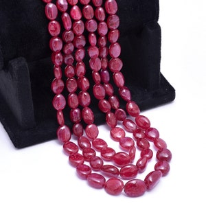 May include: A strand of red ruby gemstone beads, oval shaped, on a black velvet display stand.