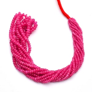 Könnte beinhalten: Eine Strähne aus rosafarbenen Edelsteinperlen, wahrscheinlich Rubine, auf einer roten Schnur aufgefädelt. Die Perlen sind klein und rund, und die Strähne ist lang genug, um als Halskette getragen zu werden.