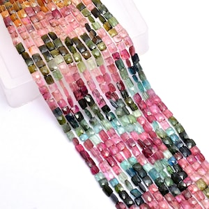 Peut inclure: Plusieurs brins de perles de tourmaline multicolores. Les perles sont rectangulaires avec des surfaces facettées, affichant une gamme de couleurs comprenant le rose, le vert, le bleu et le marron. Les perles sont enfilées, créant un aspect vibrant et texturé.