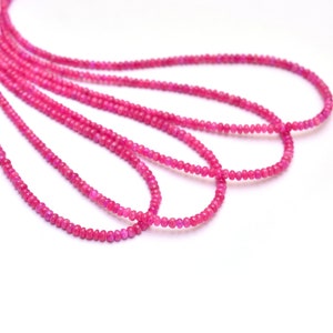 May include: A strand of pink gemstone beads, with multiple strands of beads laid out in a curved pattern on a white background.