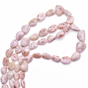 May include: A strand of pink and white fossilised coral beads. The beads are smooth and have a natural, organic shape. They are perfect for making jewellery or other crafts.