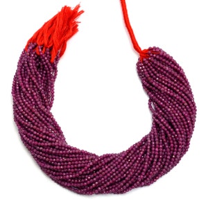 Peut inclure: Un brin de perles de pierres précieuses rouge rubis, d'environ 2 mm de diamètre, avec un pompon rouge à l'extrémité. Les perles sont facettées et ont une finition brillante et polie.