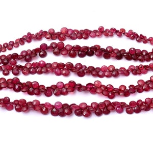 Może przedstawiać: Zbliżenie kilku sznurów głęboko czerwonych kamieni szlachetnych w kształcie łezki. Kamienie szlachetne są nawleczone, tworząc płynny wzór. Koraliki mają bogaty, nasycony kolor, a obraz jest dobrze oświetlony.