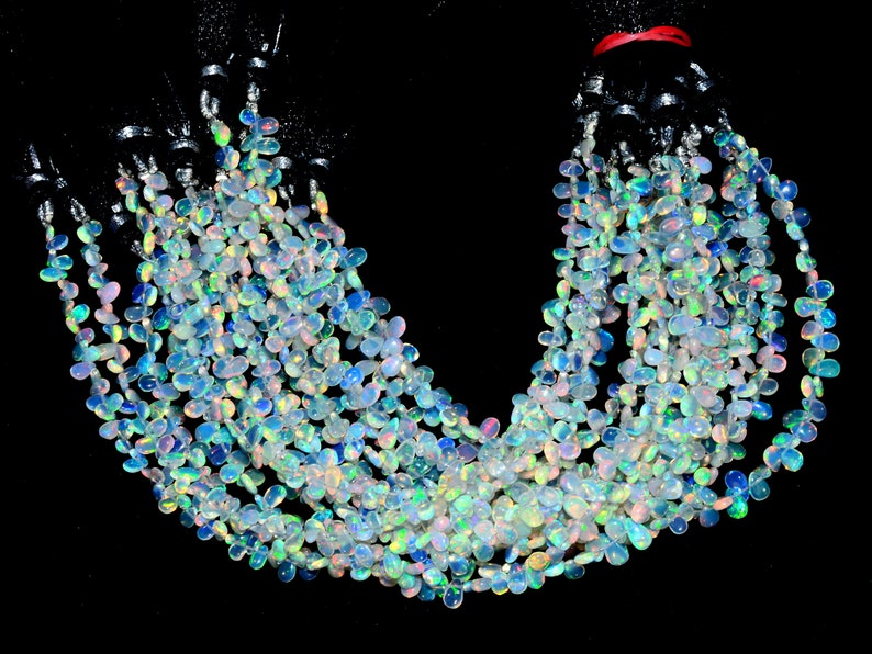 May include: A strand of iridescent opal beads in a teardrop shape. The beads are strung on a black cord and are arranged in a loose, flowing pattern.