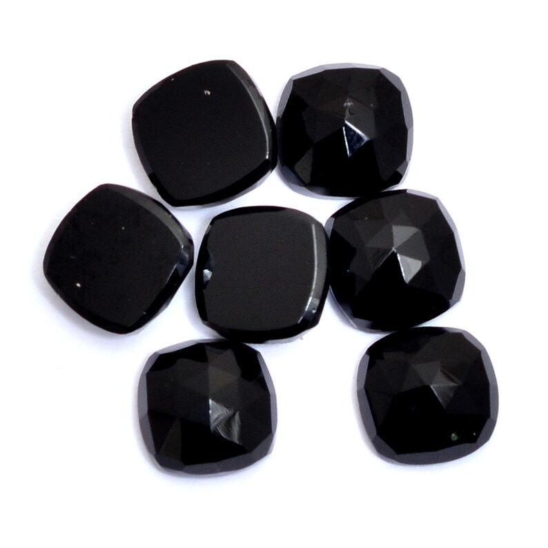 May include: Seven black gemstone cabochons in a variety of shapes and sizes. The stones are smooth and polished, with a glossy finish.