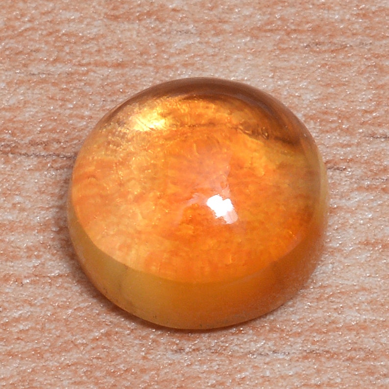 May include: A round, orange gemstone with a smooth, polished surface. The stone has a swirling, marbled pattern throughout.