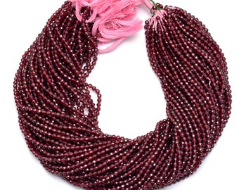 May include: A strand of deep red garnet beads, approximately 4 mm in size, strung on a thin thread. The beads are faceted and have a glossy finish. The strand is tied with a pink and green tassel.