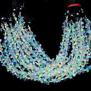 May include: A strand of iridescent opal beads in a teardrop shape. The beads are strung on a black cord and are arranged in a loose, flowing pattern.