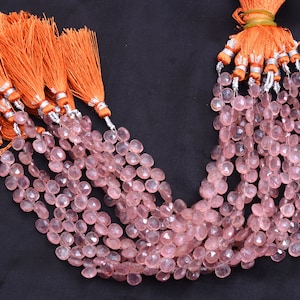 May include: Pink gemstone beads in a teardrop shape, strung together and topped with orange tassels with silver detailing. The beads are displayed against a dark background. Each bead is approximately 0.8 cm in diameter.