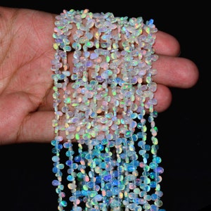 May include: A strand of iridescent white opal beads, each bead is a teardrop shape with a smooth, polished finish. The beads are strung on a clear thread and are ready to be used for jewelry making.