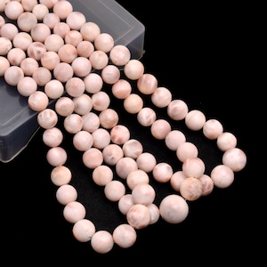 May include: A strand of pink and white gemstone beads. The beads are round and smooth, and they have a natural, organic look.