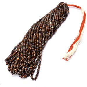 May include: A strand of brown faceted gemstone beads with iridescent flashes. The beads are strung on a white and orange thread.
