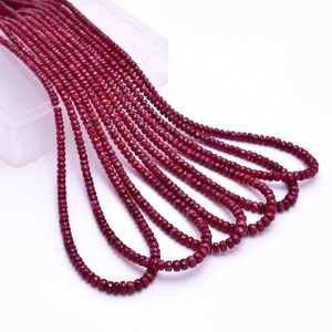 May include: A strand of deep red ruby beads, faceted and polished, arranged in a loose pile. The beads are small and uniform in size, creating a delicate and elegant look.