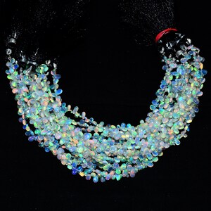 May include: A strand of iridescent opal gemstone beads, each bead is a teardrop shape with a smooth, polished finish. The beads are strung on a clear thread and are arranged in a loose, flowing pattern.