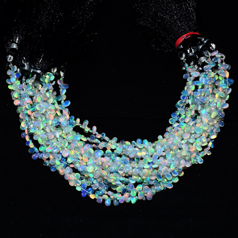 May include: A strand of iridescent opal gemstone beads, each bead is a teardrop shape with a smooth, polished finish. The beads are strung on a clear thread and are arranged in a loose, flowing pattern.