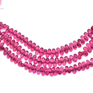 May include: A strand of pink faceted gemstone beads. The beads are strung on a silver wire and are arranged in a curved shape.