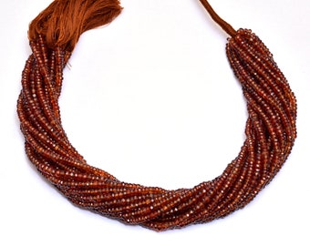May include: A necklace made of multiple strands of small, faceted, reddish-brown beads. The beads are tightly strung, creating a curved shape. A brown tassel and cord are attached at one end.