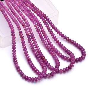 May include: A strand of pink ruby beads, with multiple strands of beads laid out in a row. The beads are round and smooth, and they have a slightly translucent appearance.