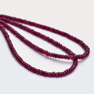 Puede incluir: Múltiples hilos de pequeñas cuentas redondas de rubí rojo intenso. Las cuentas están ensartadas, formando collares. Las piedras preciosas tienen un aspecto pulido y se muestran sobre un fondo blanco.