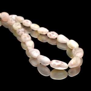 May include: A strand of pale pink and white oval-shaped beads, strung together to form a necklace. The beads have a smooth, polished finish and a subtle shimmer.
