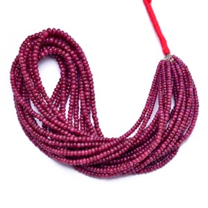 Puede incluir: Un collar de pequeñas cuentas redondas de rubí rojo oscuro. Las cuentas están ensartadas, formando múltiples hebras que se juntan en la parte superior con un hilo rojo. Las cuentas tienen un aspecto pulido y brillante.