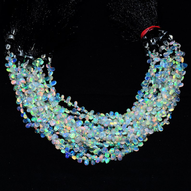 May include: A strand of iridescent opal gemstone beads, each bead is a teardrop shape with a smooth, polished finish. The beads are strung on a clear thread and are arranged in a loose, flowing pattern.