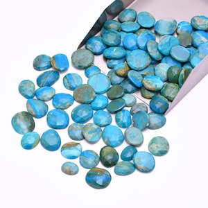 May include: A collection of polished turquoise gemstones in various shapes and sizes, with a faceted cut. The stones range in color from light to deep blue, with some showing green and brown veining. They are displayed on a white surface.