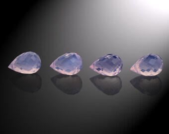 May include: Four teardrop-shaped, faceted, pale pink gemstones with a slight purple hue. The gemstones are arranged in a row on a black surface.