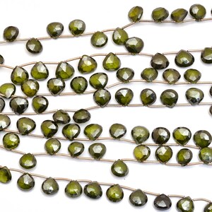 May include: A strand of dark green gemstone beads, each bead is faceted and shaped like a teardrop. The beads are strung on a silver wire.
