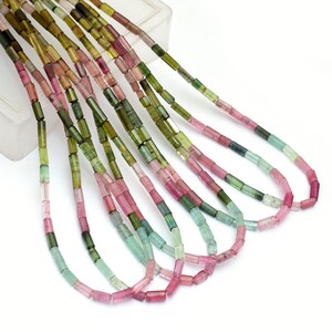 May include: A strand of multi-coloured tourmaline beads. The beads are faceted and have a rectangular shape. The colours of the beads are pink, green, and blue.