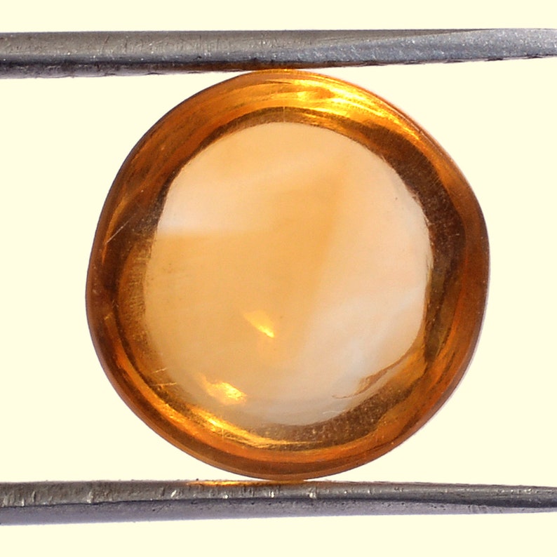 May include: A round, orange gemstone with a white center, held in tweezers.